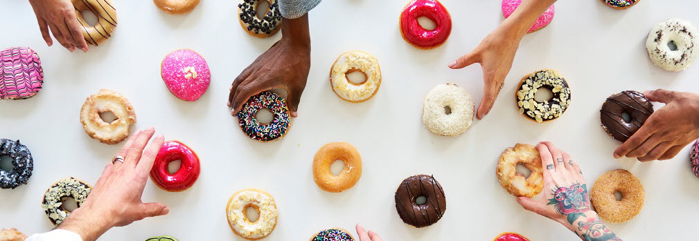 Hands reaching for a table full of donuts