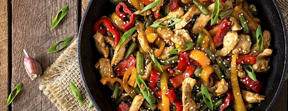Sautee pan with a cooked stir fry dish including colorful veggies, and chicken slices.