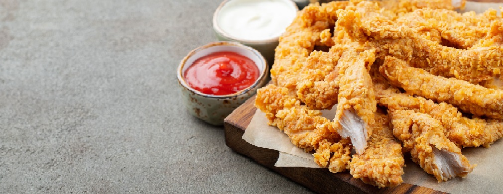 Wood cutting board with fried chicken tenders on top and sides of dipping sauce and French fries
