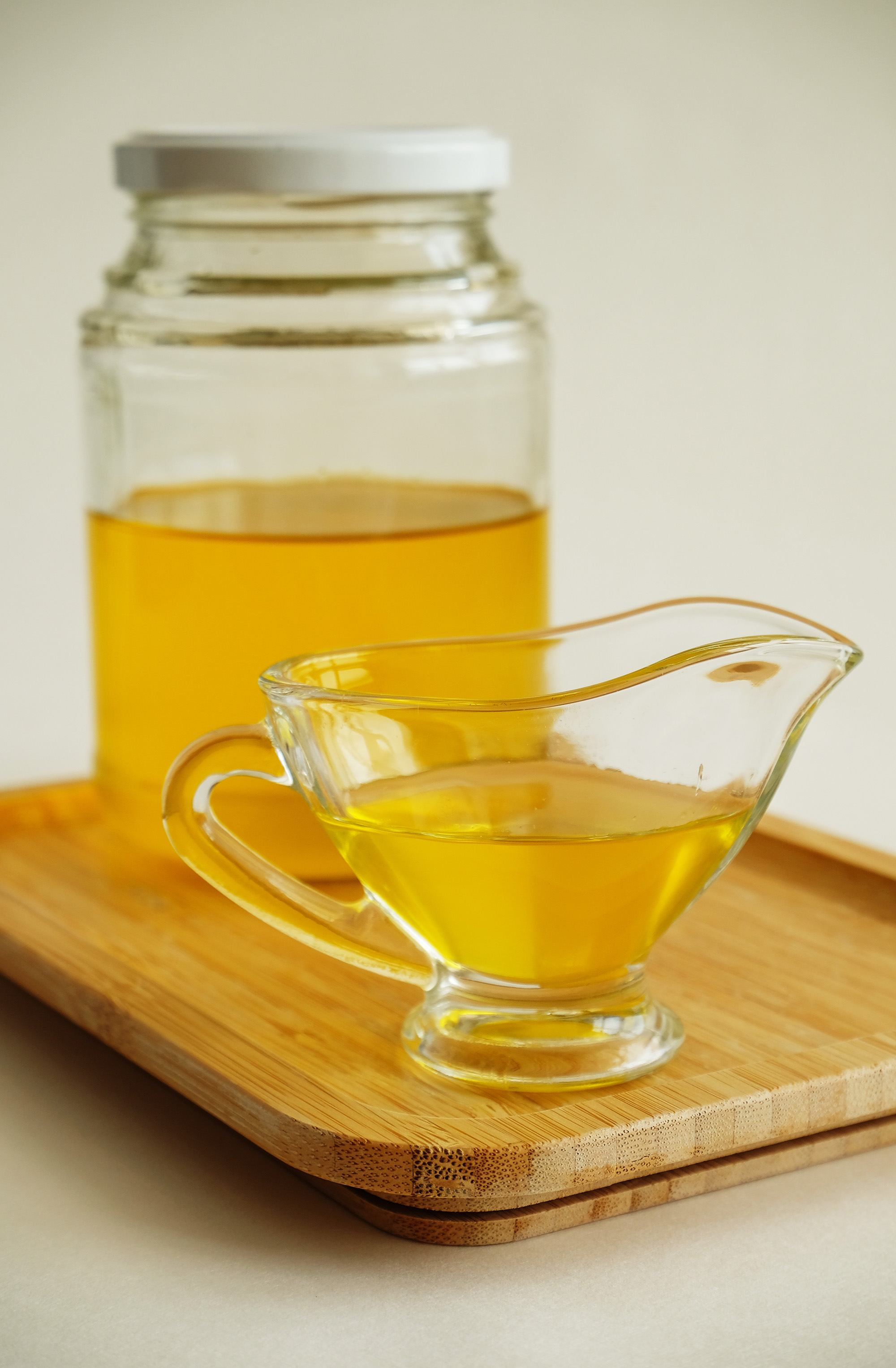 Golden liquid butter in a glass gravy boat sitting in front of a glass jar of the same.
