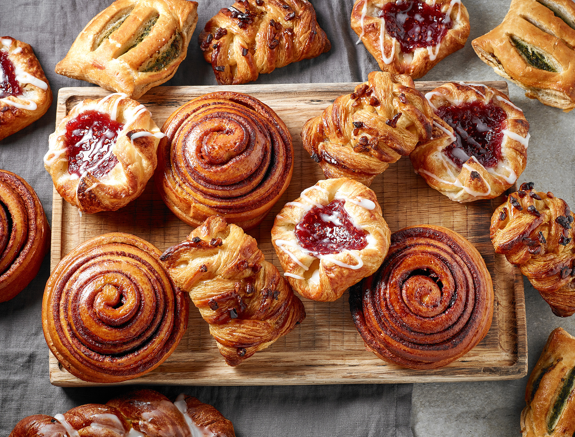 A platter of Danishes and rolls on a wood cutting board. 