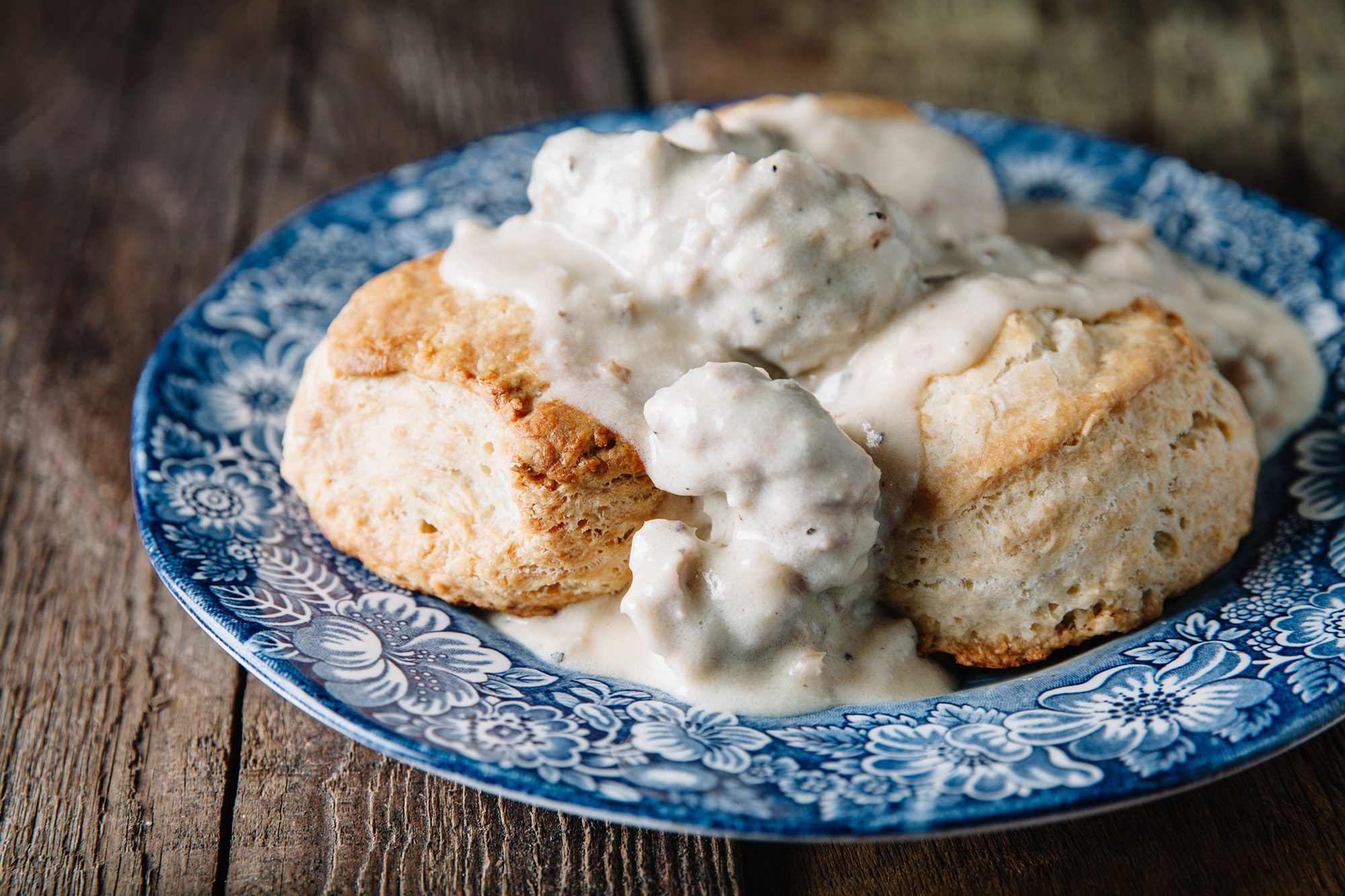 Biscuits and gravy served on a blue floral-rimmed plate. 