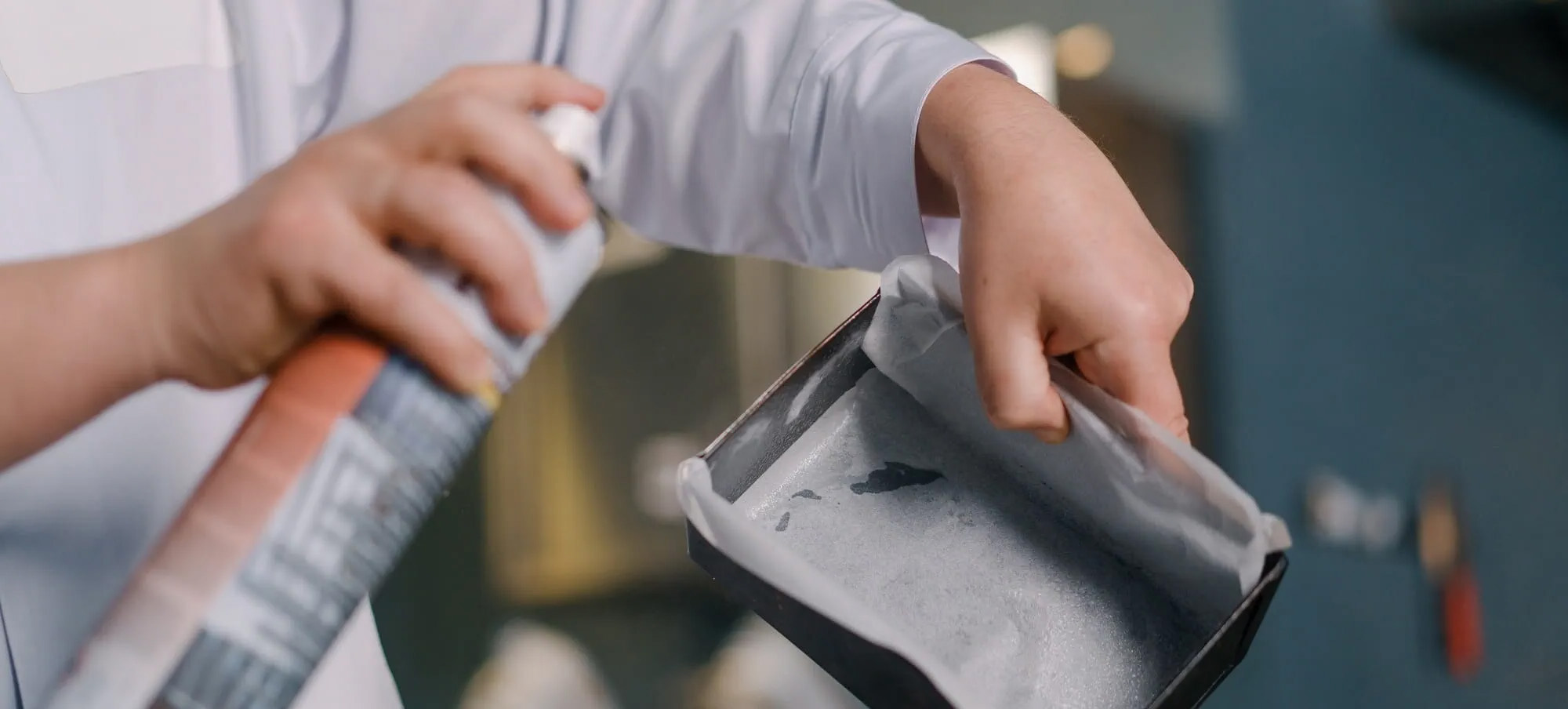 Close up of the arms of a chef spraying a pan with cooking spray