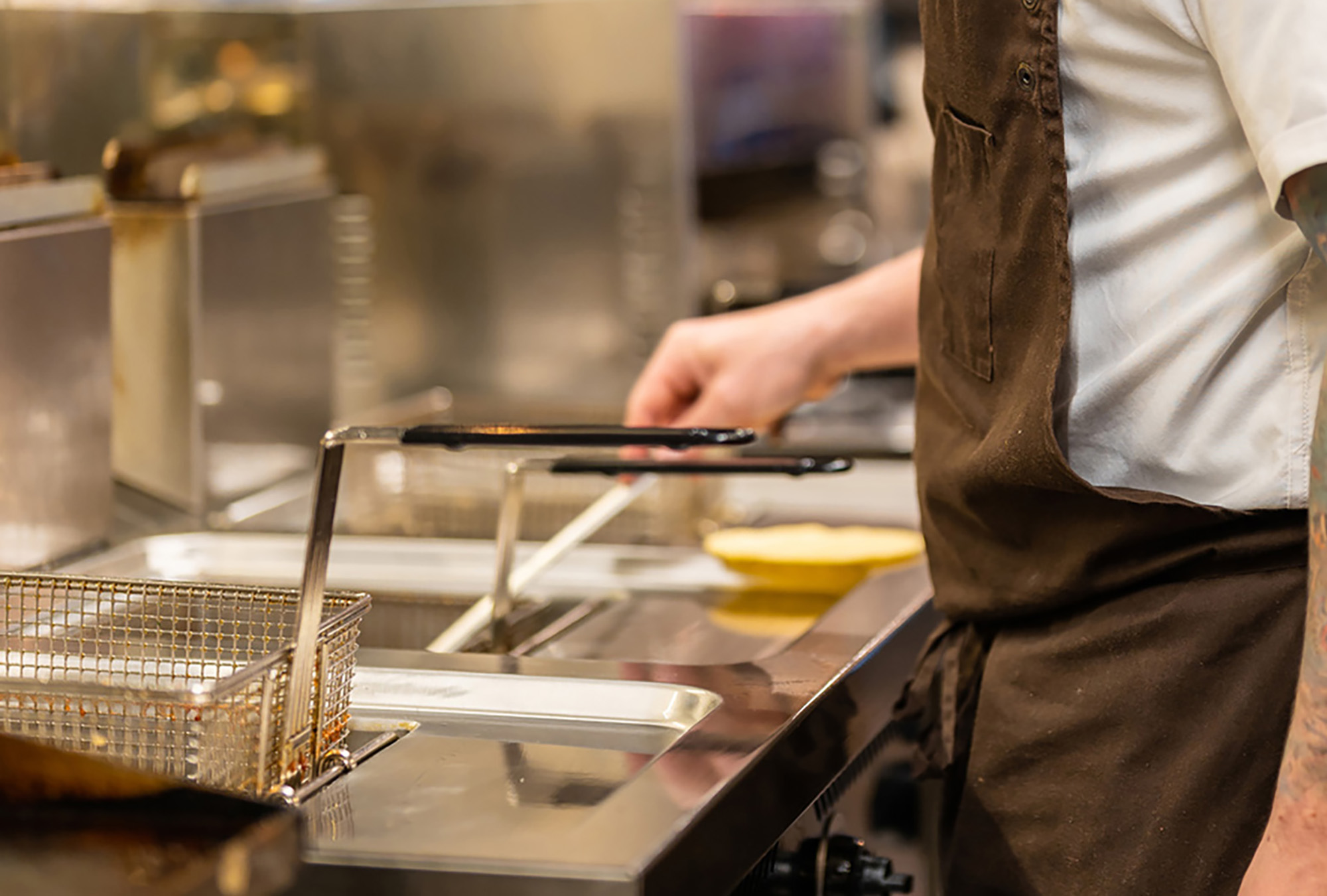 Close up of deep fryer baskets with a person grabbing one.
