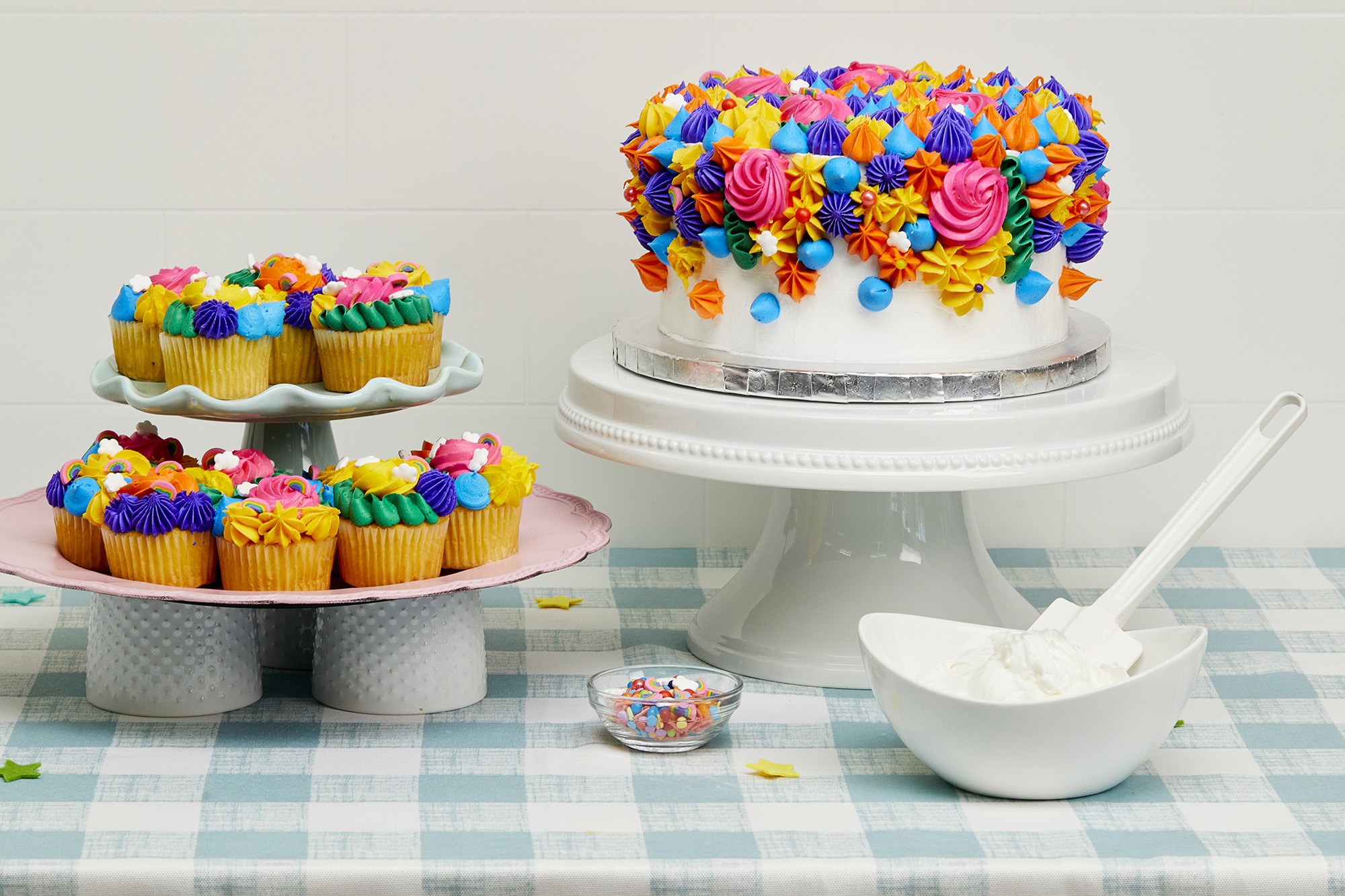Colorful cupcakes on a tiered platter in the foreground with colorful cake in the background. 