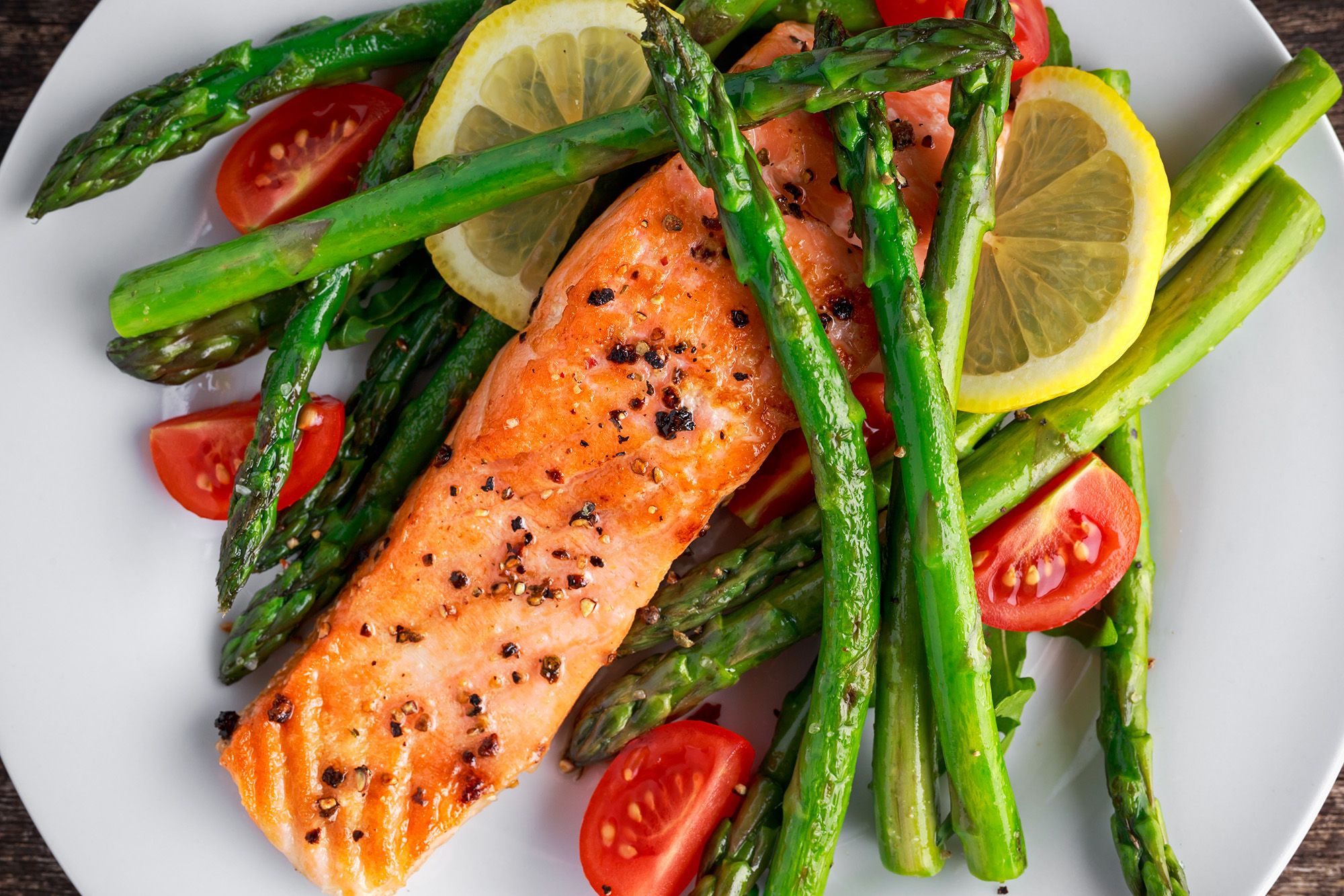 A close-up plate of salmon, asparagus, and cherry tomatoes sliced.