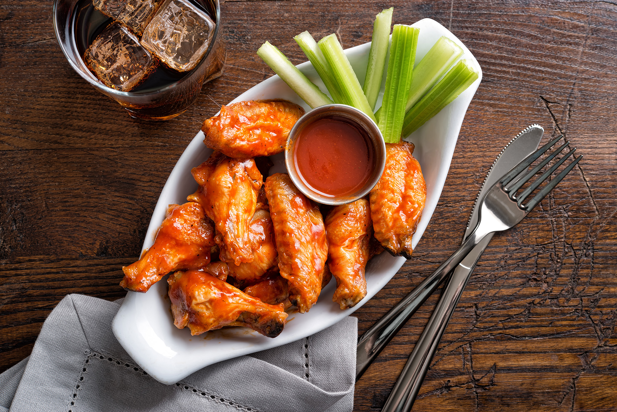 Overhead shot of a boat of bbq chicken wings, sauce and celery.