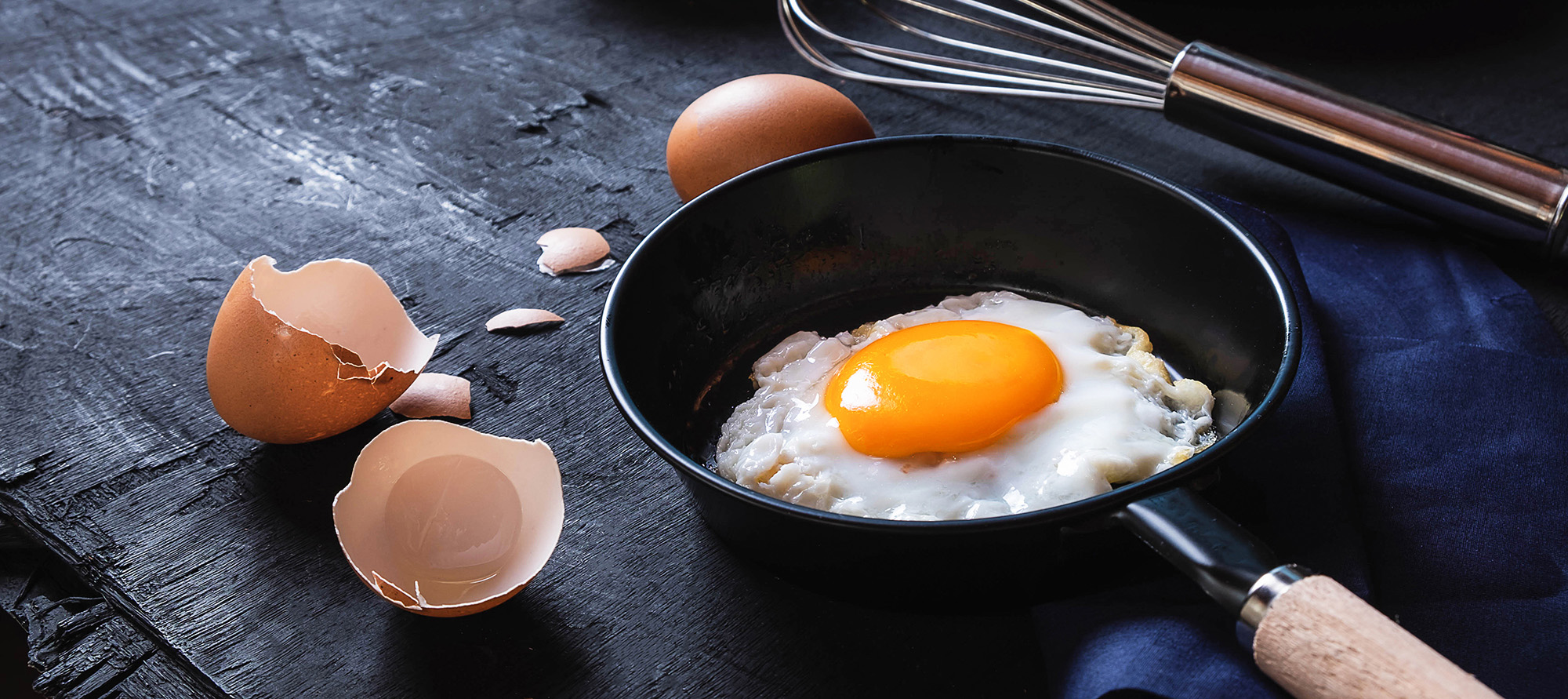 A fried egg sitting in the pan it was cooked in. Cracked eggshells sit next to it.