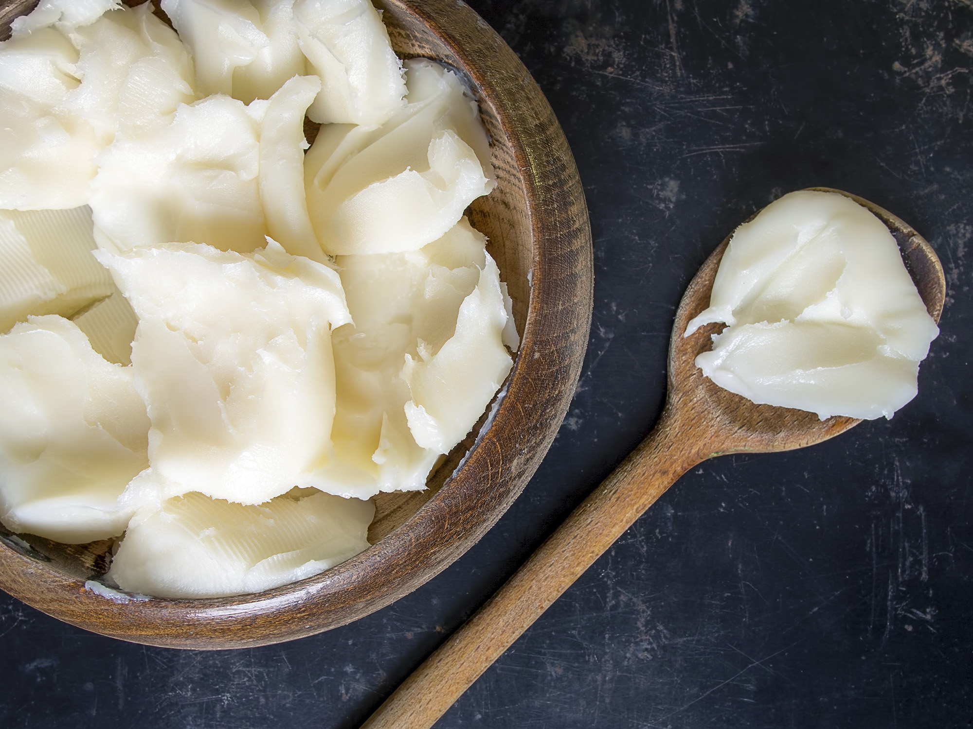 Wooden bowl filled with white shortening and a wooden spoon resting at its side.