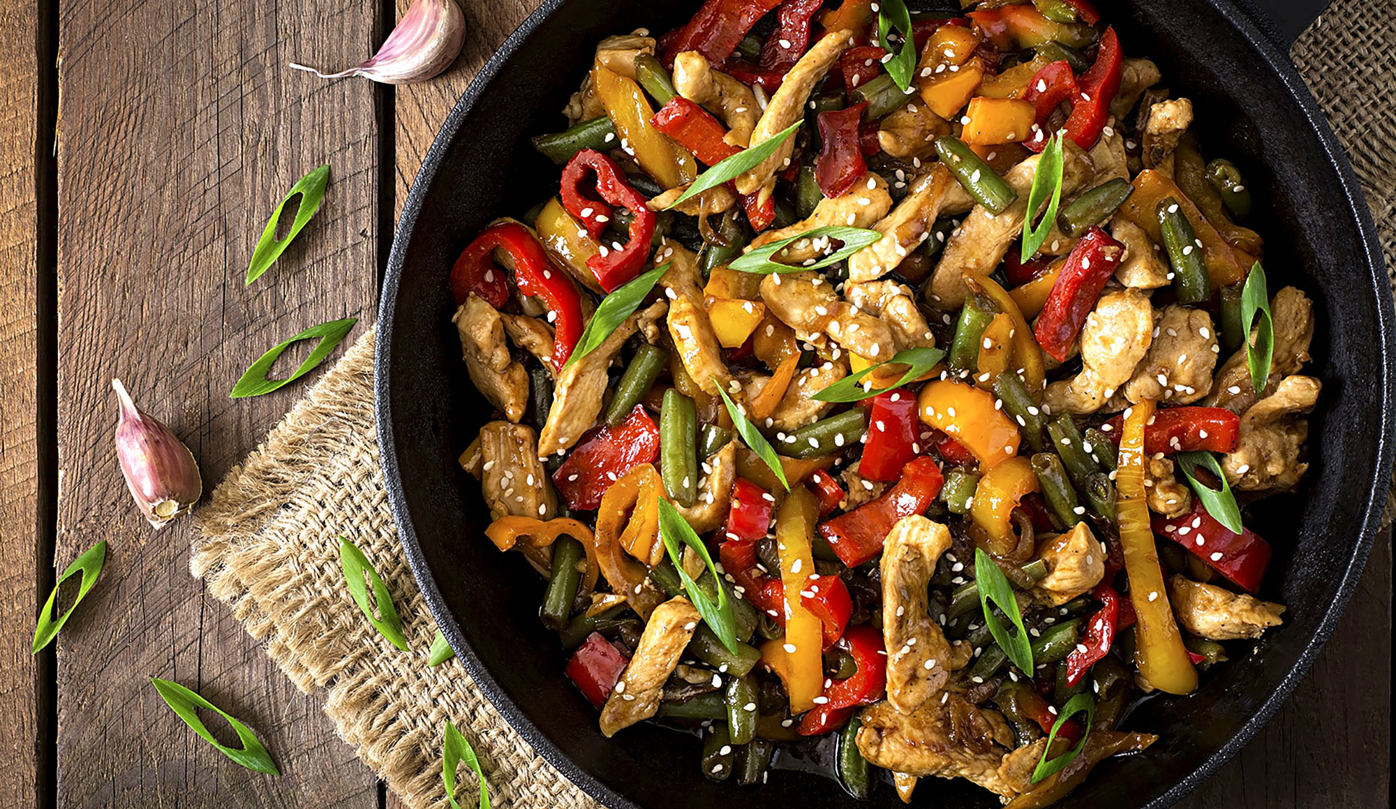 Sautee pan with a cooked stir fry dish including colorful veggies, and chicken slices. 