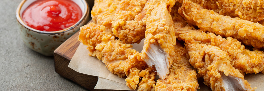 Wood cutting board with fried chicken tenders on top and sides of dipping sauce and French fries. 